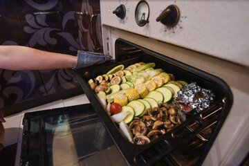 Woman hands putting tray with fresh vegetables into the oven for grill. Selective focus. Low DOF.