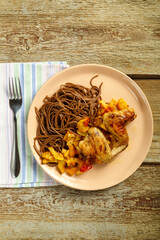 Beige plate of soba noodles with vegetables and chicken wings on a napkin and a fork.