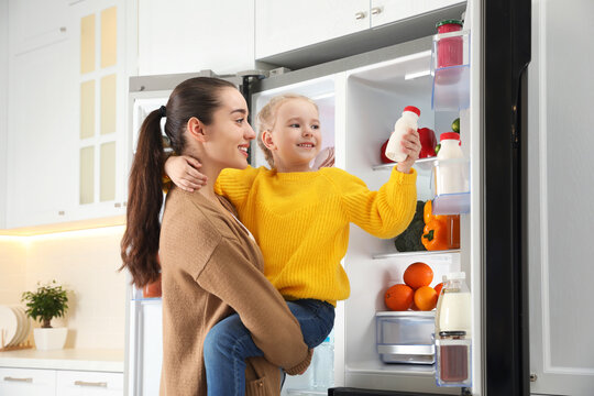 Young Mother And Daughter Near Open Refrigerator In Kitchen