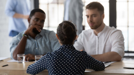 Rear view two diverse hr managers holding job interview with young Indian woman candidate, sitting at desk in modern office, asking questions, hiring process, employment and recruitment