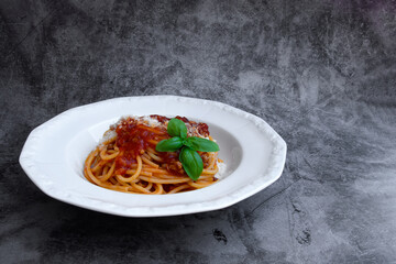 White plate with a portion of delicious italian spaghetti with fresh basil leaves and grated parmesan cheese on the cement background, front view, copy space
