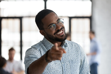 Head shot portrait close up smiling African American hr manager wearing glasses pointing finger at you, looking at camera, overjoyed employer recruiter choosing job candidate, hiring process