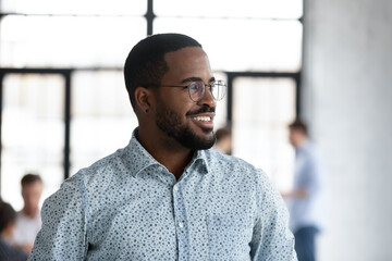 Close up smiling dreamy African American businessman wearing glasses looking to aside, business vision concept, positive executive company owner dreaming, pondering project strategy or startup idea - obrazy, fototapety, plakaty