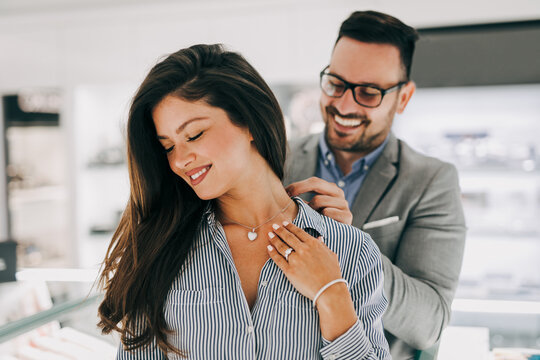 Middle Age Couple Enjoying In Shopping At Modern Jewelry Store. Young Woman Try It Out Gorgeous Necklace And Earrings.