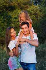beautiful family, mom, dad and daughter play with Holly colors. multi-colored paint on clothes and face