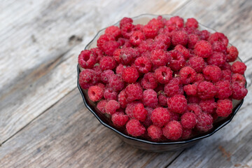 Raspberries in a glass bowl on a wooden rustic table. Useful forest berry in the village.