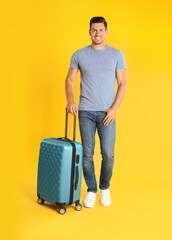 Handsome man with suitcase for summer trip on yellow background. Vacation travel