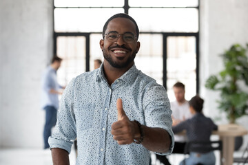 Head shot portrait smiling African American businessman wearing glasses showing thumb up, looking...