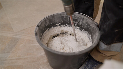 Mix the mixture in a black bucket. Worker mixes a solution in a black bucket. A man mixes a white mixture in a bucket. White substance in a black bucket.