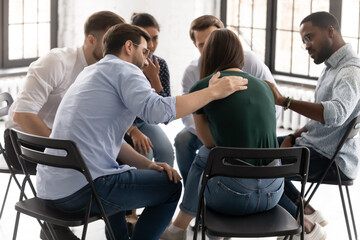Rear view diverse people supporting frustrated upset woman feeling pain, sitting in circle at group...