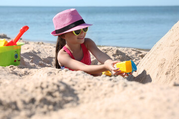 Cute little child playing with plastic toys at sandy beach on sunny day