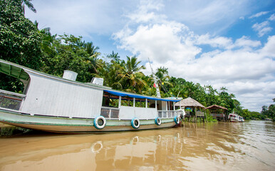 Embarcação de madeira ancorada em trapiche em um rio da floresta amazônica. Barco na margem de...