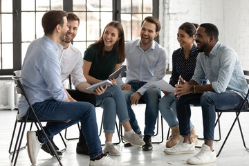 Happy diverse colleagues laughing at joke, having fun at briefing, sitting on chairs in modern...