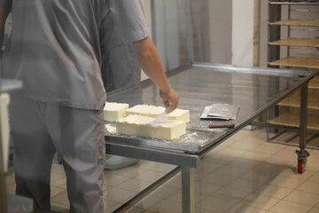 Worker salting fresh cheese at modern factory, closeup