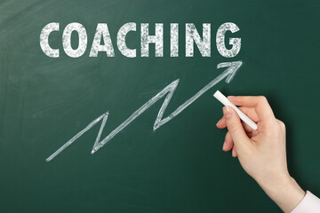 Business or life trainer drawing arrow under word Coaching on green chalkboard, closeup