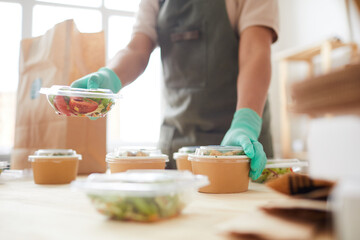 Close up of unrecognizable female worker wearing protective gloves while packaging orders at food delivery service, copy space