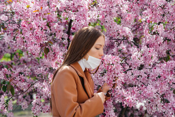 A young girl takes off her mask and breathes deeply after the end of the pandemic on a Sunny spring day, in front of blooming gardens. Protection and prevention covid 19