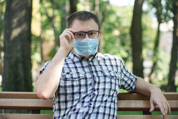 Fototapeta premium The guy in the mask from the virus sits on a park bench