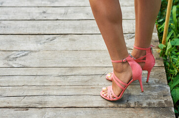 Tanned legs of a girl in summer sandals with coral-colored heels.