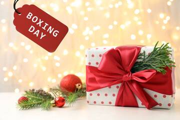 Gift and tag with text Boxing day against blurred Christmas lights