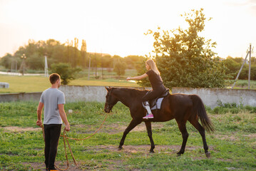 A young and pretty girl is learning to ride a thoroughbred Mare on a summer day at the ranch. Horse...