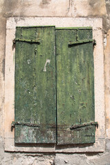 Old distressed green painted wooden shutters covering a stone framed window