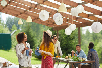 Wide angle view at multi-ethnic group of friends preparing for Summer party at outdoor terrace,...