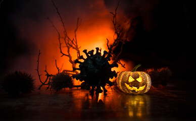 Halloween during Corona virus global pandemic concept. Glowing pumpkins and Covid novel on dark with thematic spooky decorations. Halloween pumpkin on foggy backlight.