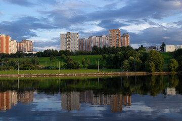 Fototapeta na wymiar View from the river to the green embankment and residential area of Moscow against the background of a beautiful sky with clouds.