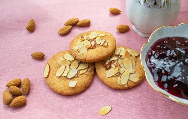 Composition in natural sunlight. Homemade gingerbread cookies with almond petals, a handful of nuts and a bowl of jam. Against the background of pink linen fabric