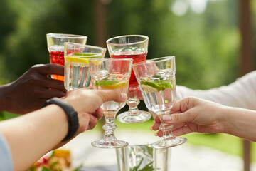 Close up of multi-ethnic group of friends clinking cocktail glasses while enjoying outdoor party in...
