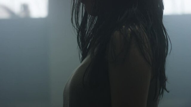Contemporary dancer with eyes closed leans back, whips her hair begins to dance with passion and energy in slow motion surrounded by mist in industrial warehouse