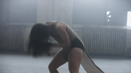 Beautifiul dancer whips her hair, kicks dancing with lots of energy and passions surrounded by mist in industrial warehouse