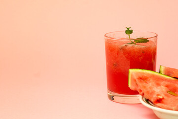 Delicious red watermelon juice with sliced fruit pieces on a plate. A sprig of mint in a glass. Copy space. Summer food concept