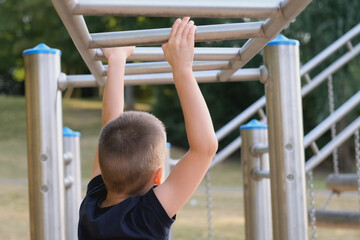 Obraz premium boy, kid walking on an incline on the playground, rear view, concept of physical activity, children's sports, balance