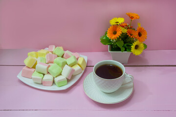 Cup of coffee and plate of colored marshmallows on pink wooden table. Concept of tenderness,...