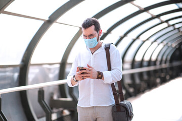 An authentic looking Turkish young man is walking over an isolated footbridge and checking his mobile phone with his protective mask