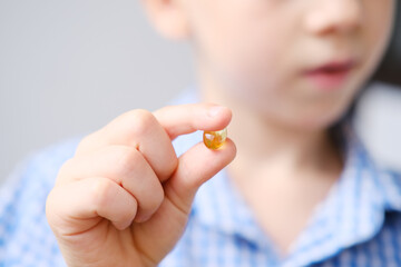 boy kid holds a capsule with fish oil in gelatin in his hand, the concept of children's health,...