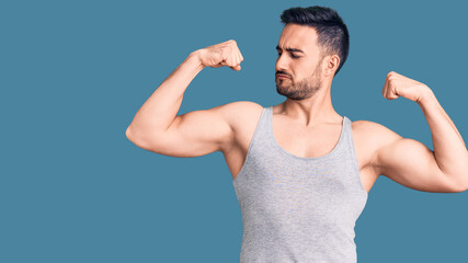 Young handsome man wearing swimwear and sleeveless t-shirt showing arms muscles smiling proud....