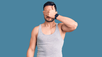 Fototapeta premium Young handsome man wearing swimwear and sleeveless t-shirt covering eyes with hand, looking serious and sad. sightless, hiding and rejection concept