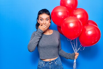 Young woman holding balloons covering mouth with hand, shocked and afraid for mistake. surprised expression