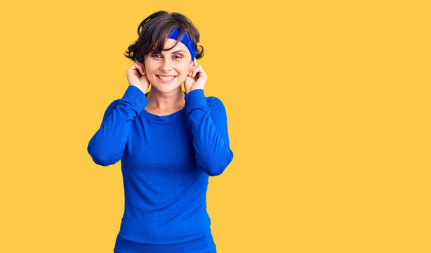 Beautiful young woman with short hair wearing training workout clothes smiling pulling ears with fingers, funny gesture. audition problem