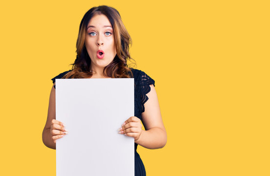 Young beautiful caucasian woman holding cardboard banner with blank space scared and amazed with open mouth for surprise, disbelief face