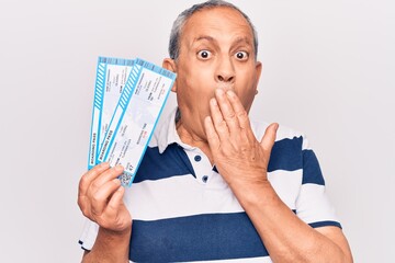 Senior handsome grey-haired man holding airline boarding pass over isolated white background covering mouth with hand, shocked and afraid for mistake. Surprised expression