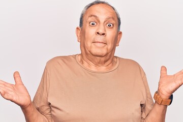 Senior man with grey hair wearing casual t-shirt clueless and confused with open arms, no idea and...