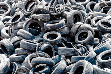 Assorted pile of old and used automotive road tires, showing a variety of tread patterns in a tires...