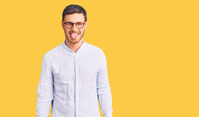 Handsome young man with bear wearing elegant business shirt and glasses sticking tongue out happy with funny expression. emotion concept.