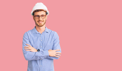 Handsome young man with bear wearing architect hardhat happy face smiling with crossed arms looking at the camera. positive person.