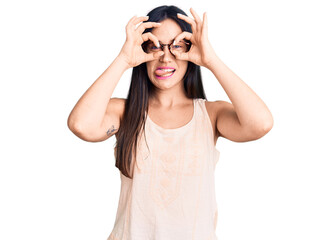 Young beautiful caucasian woman wearing casual clothes and glasses doing ok gesture like binoculars sticking tongue out, eyes looking through fingers. crazy expression.