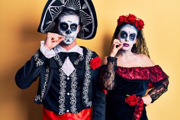 Obraz premium Young couple wearing mexican day of the dead costume over yellow mouth and lips shut as zip with fingers. secret and silent, taboo talking
